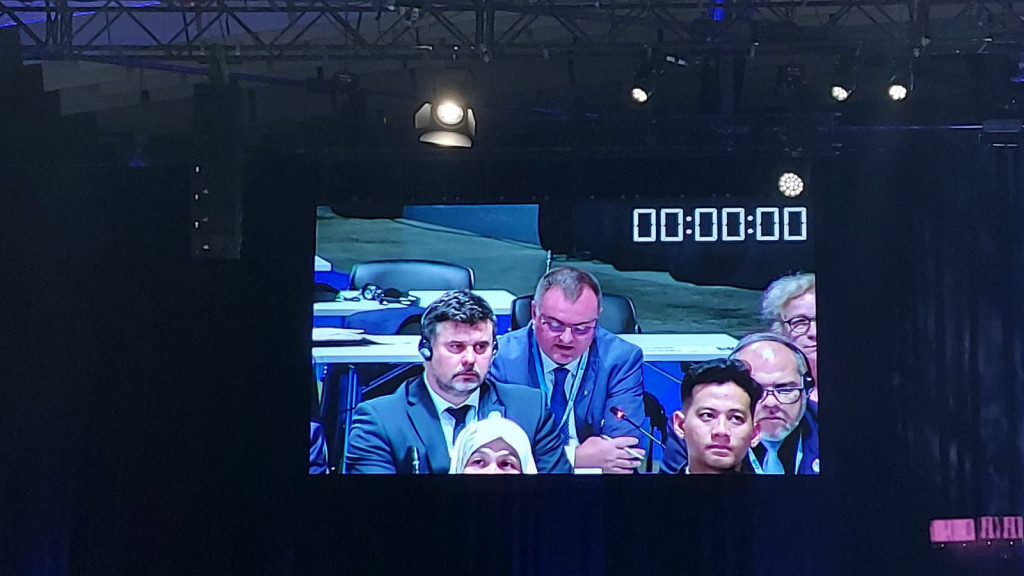 Photo of a screen with a few people, one of them is speaking 