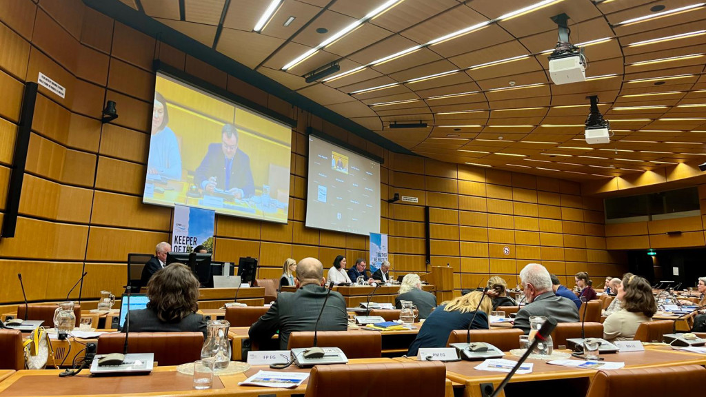 Full conference room, with a man's face on the screen 