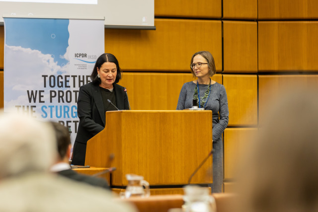 Two women stand together to speak at a meeting