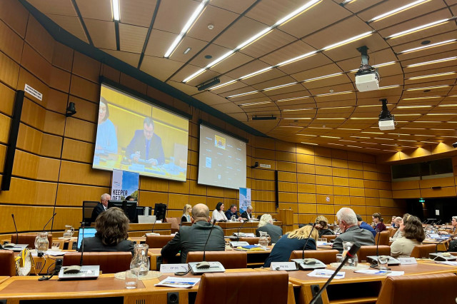 Full conference room, with a man's face on the screen 