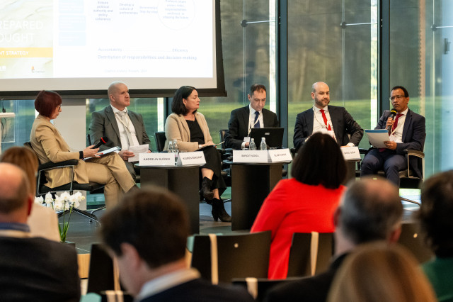 six persons sitting on a panel in front of an audience